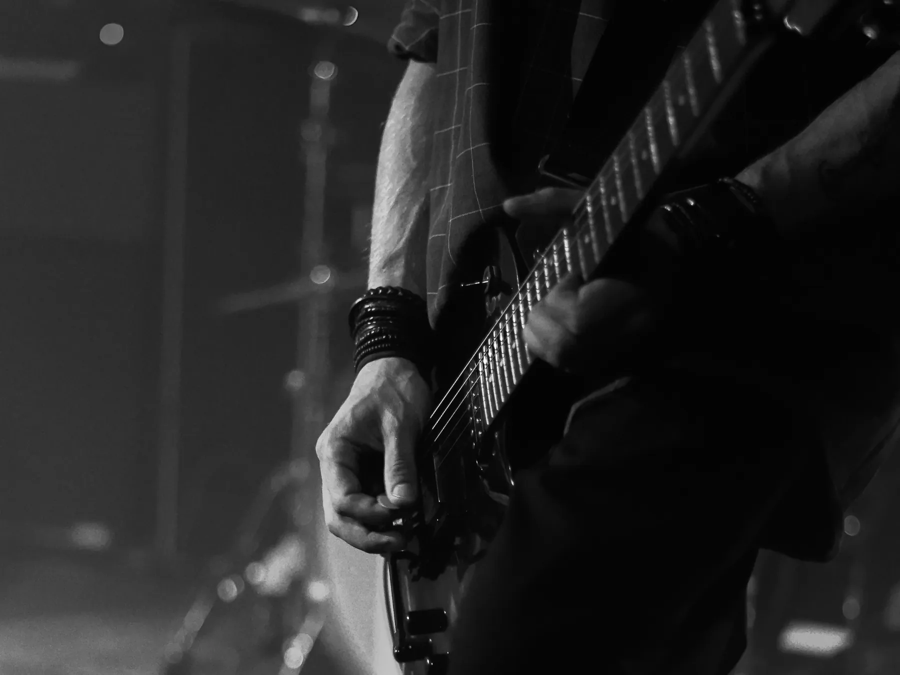 Close-up of a guitarist’s hand on an electric guitar in black and white.