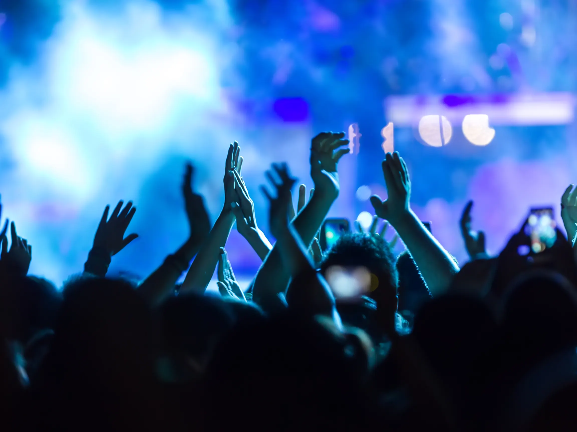 Audience members raising their hands beneath blue concert lighting.