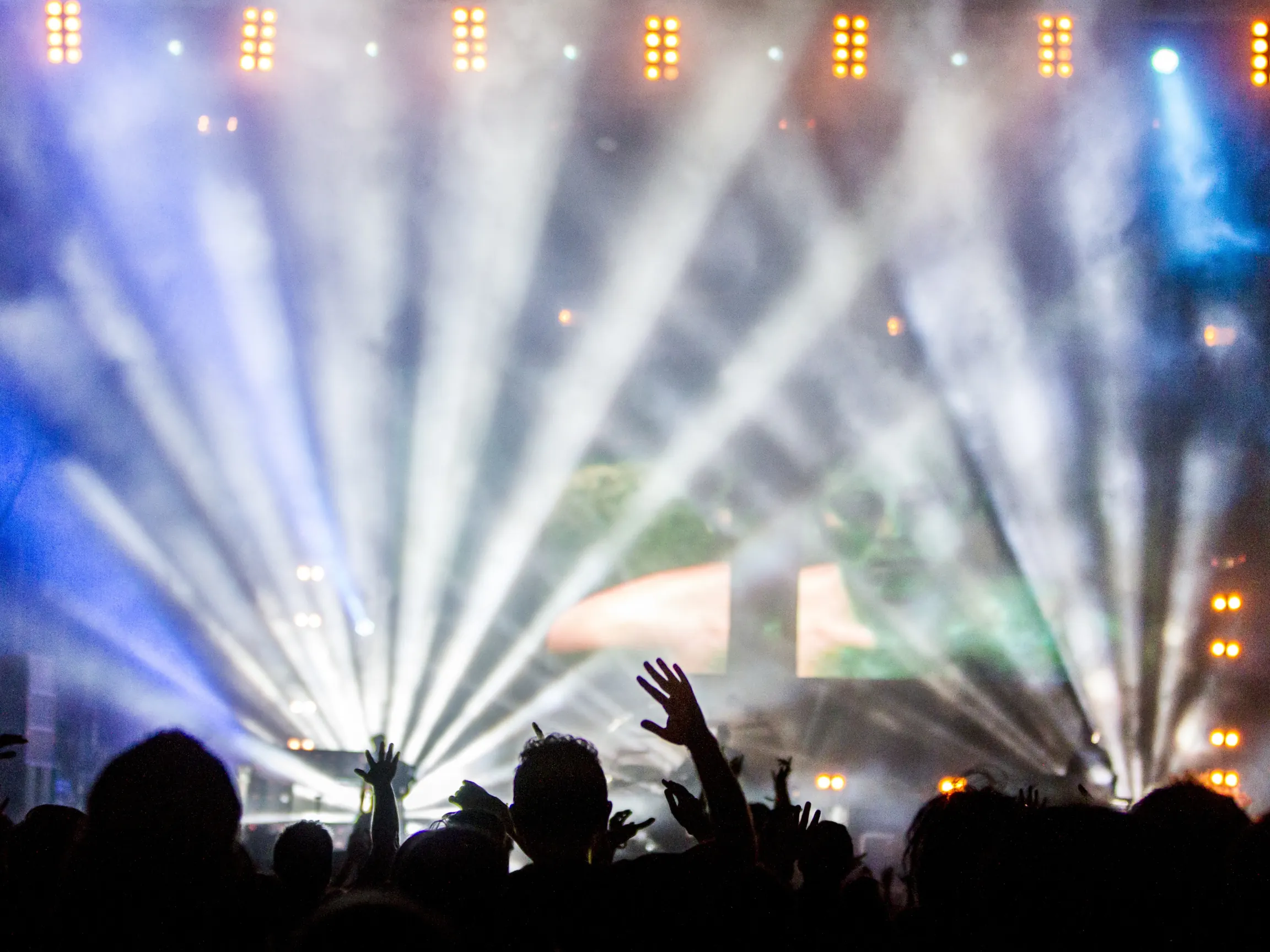 Stage lights over an audience, silhouetted against a live performance.