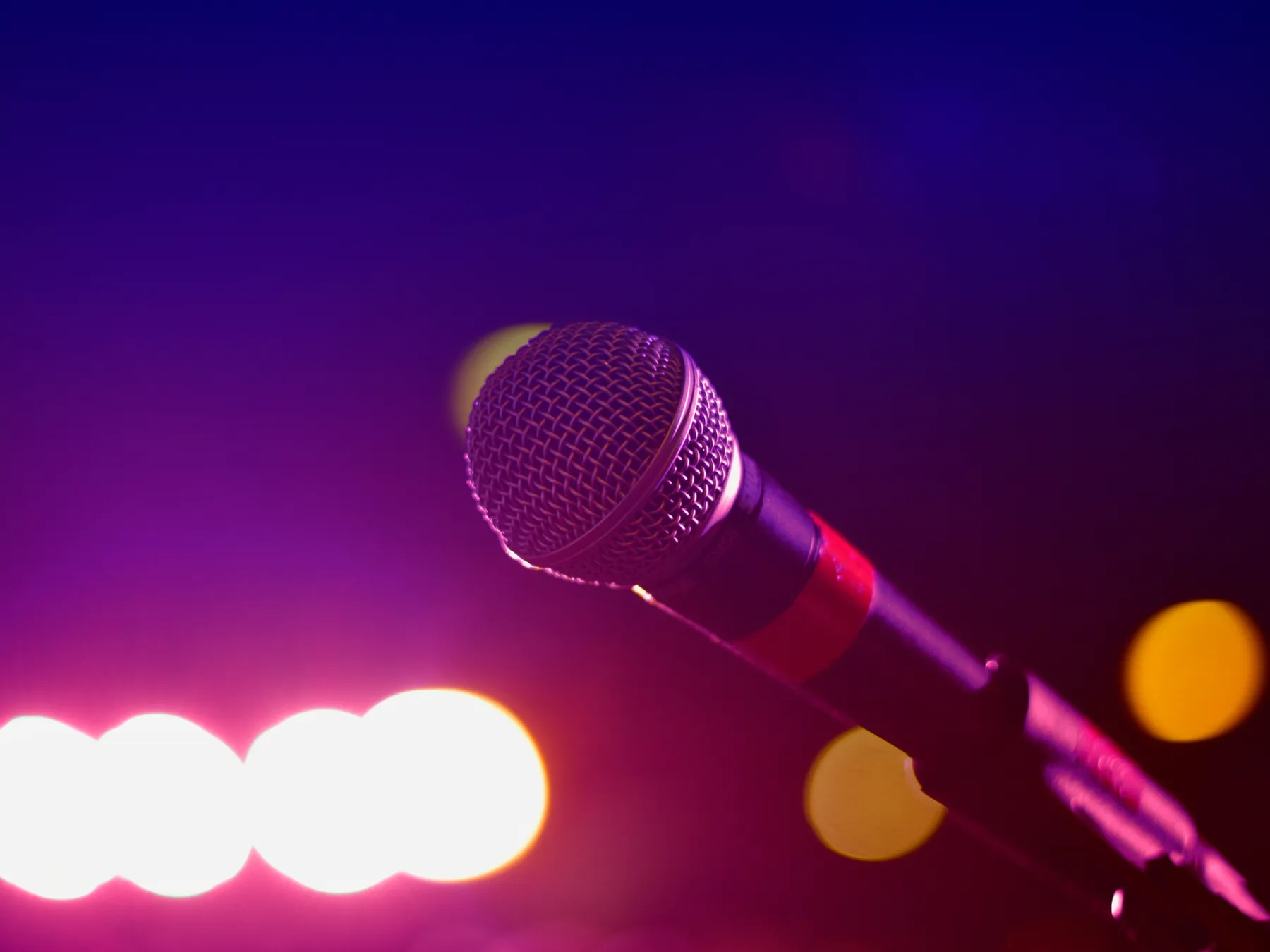 A stage microphone against violet lighting.
