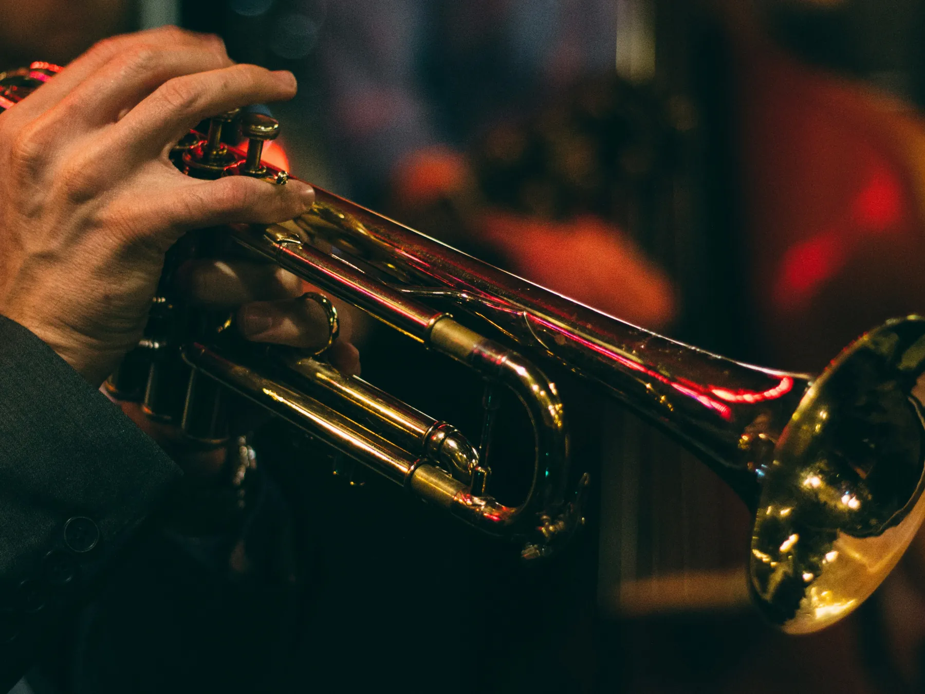 A hand holding a gold trumpet under warm stage light.