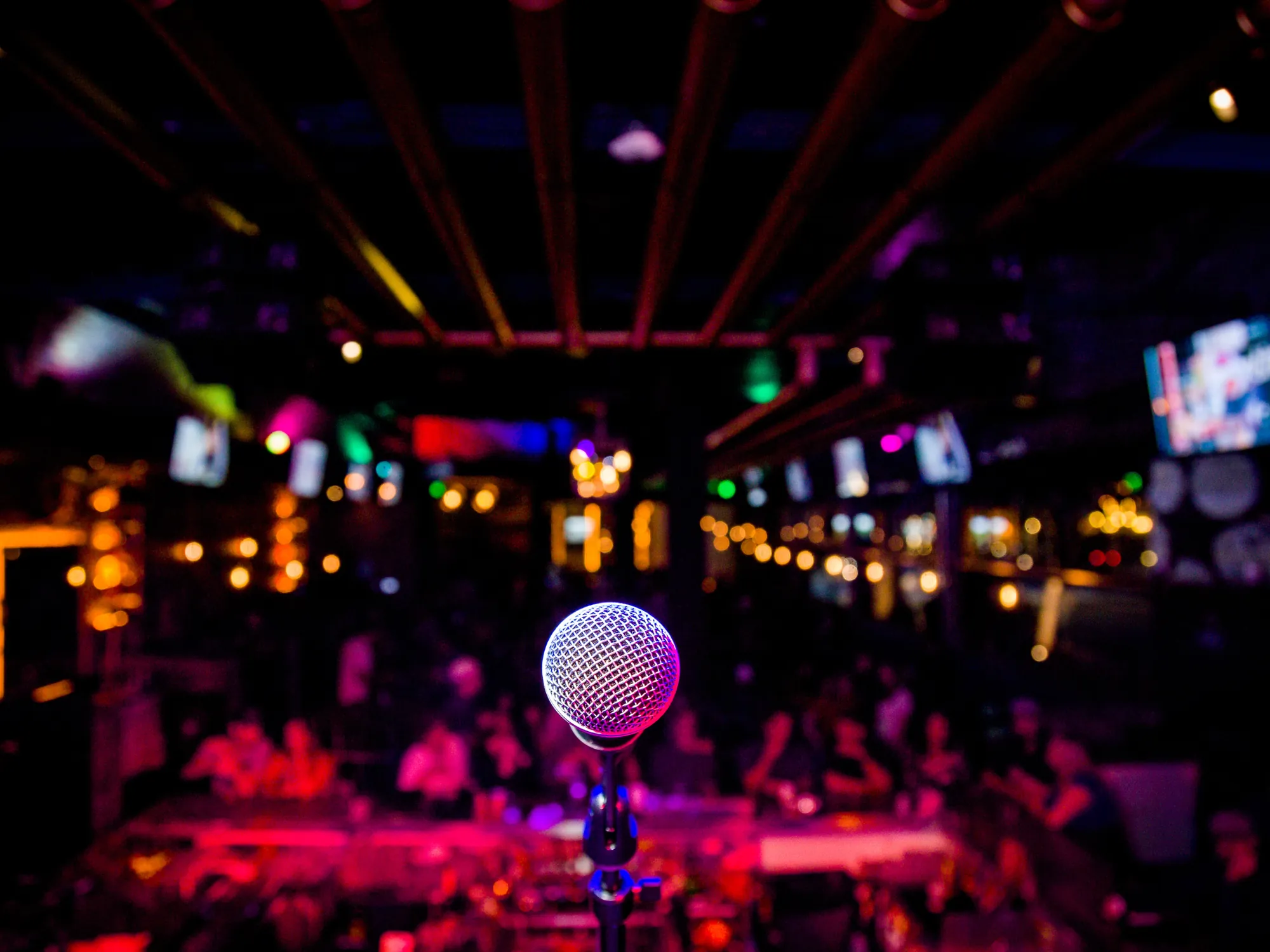 A microphone on a darkened stage before a seated audience.